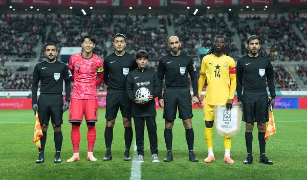 하나은행이 한국과 가나의 축구대표팀 A매치 경기에서 이주배경가정 아동들에게 ‘매치볼 키드’와 ‘기수단’으로 참여하는 체험기회를 제공했다. 기수단 아동•청소년들은 국기를 들고 경기장에 입장했으며, 매치볼키드가 주심에게 볼을 전달한후 손흥민 선수 등 양팀 주장 및 심판진과 기념촬영을 하고 있다. (사진=하나은행) 